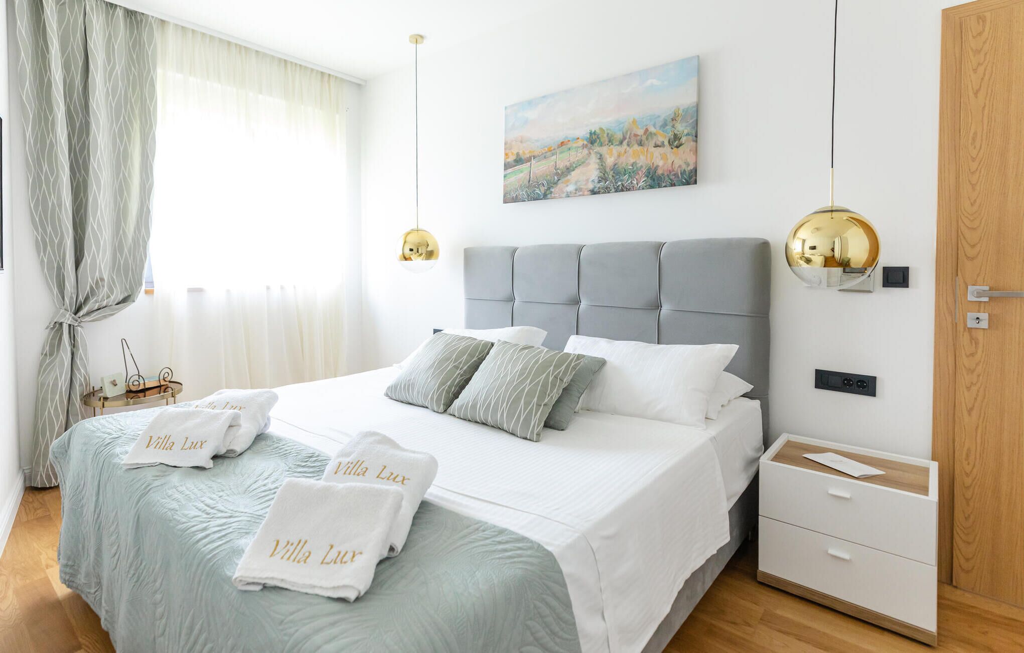 Une chambre à coucher bien rangée, avec un grand lit, des tables de chevet, une lampe de chevet et un tableau accroché au mur.