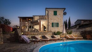 Eine Steinvilla mit Swimmingpool, Sitzgelegenheiten im Freien und einer Pergola.