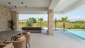 An outdoor patio with a dining table and chairs, a built-in seating area, a pool, and a view of the landscape. - Beautiful home in Nin (Nin)