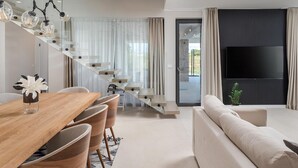 A modern living room with a sofa, a dining table with chairs, a staircase, and a TV mounted on the wall. - Beautiful home in Nin (Nin)