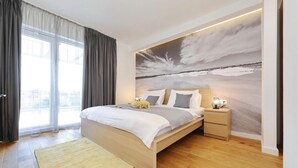 A modern bedroom with a large bed, a nightstand, a wall-mounted lamp, and a view of a snowy landscape through the window. - Luxurious home in Zaton (Zaton)