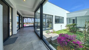 Une maison moderne avec de grandes fenêtres en verre, une terrasse agrémentée de plantes et une vue sur la mer.
