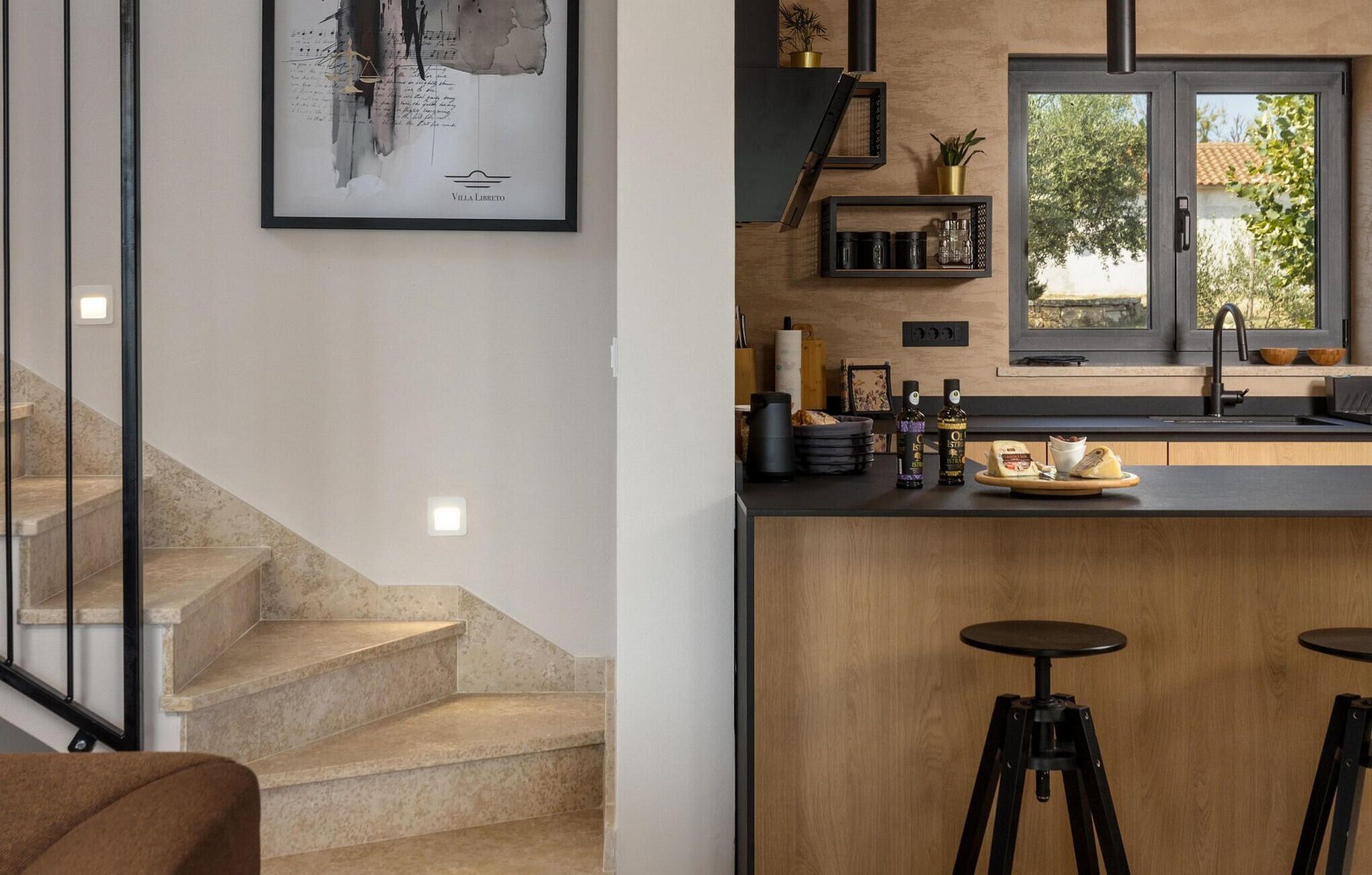 Uma cozinha moderna com bancada de madeira, banquetas, uma janela com vista e uma escada.