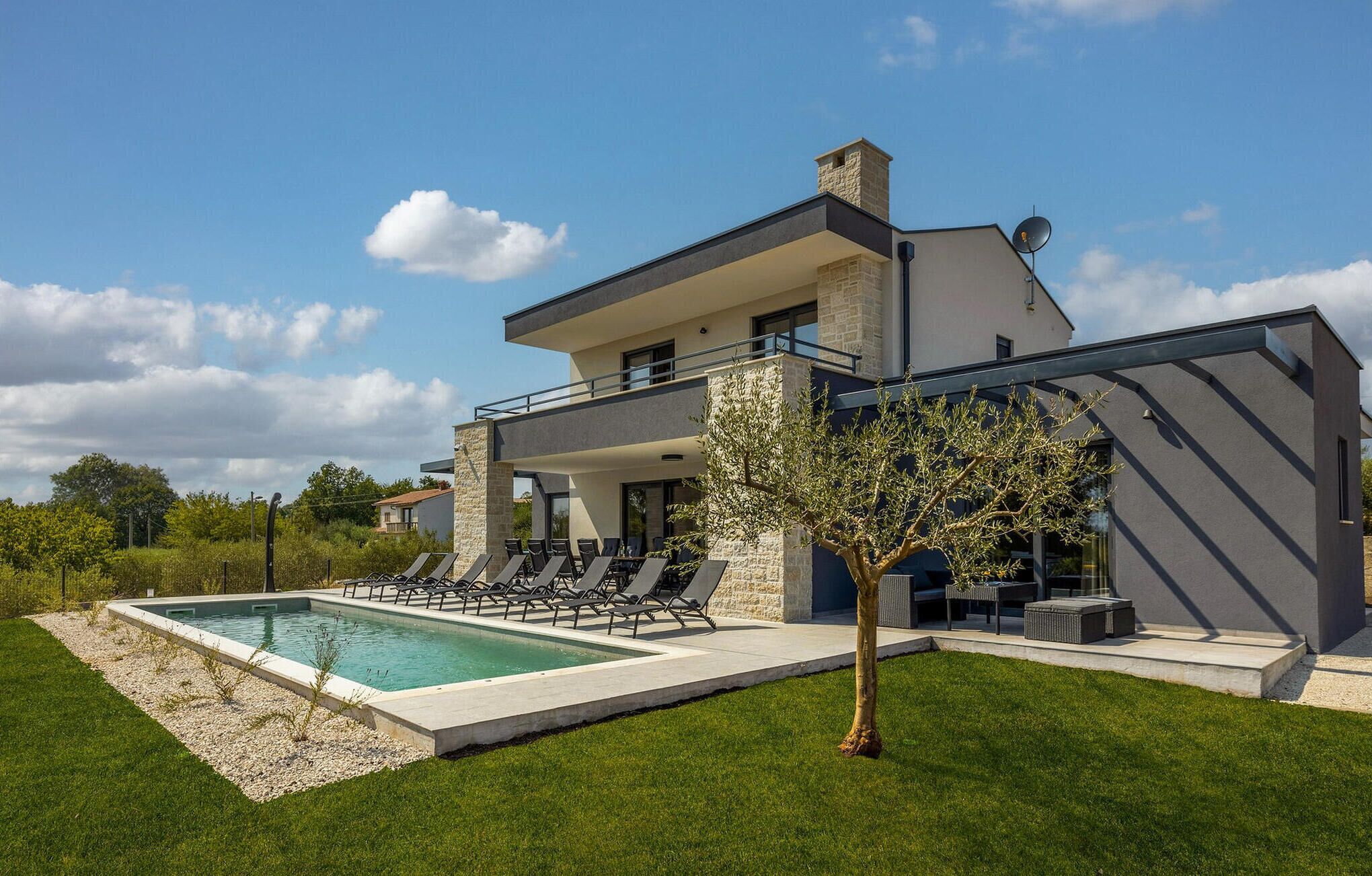 Una casa moderna de dos pisos con piscina, mobiliario exterior y un árbol.