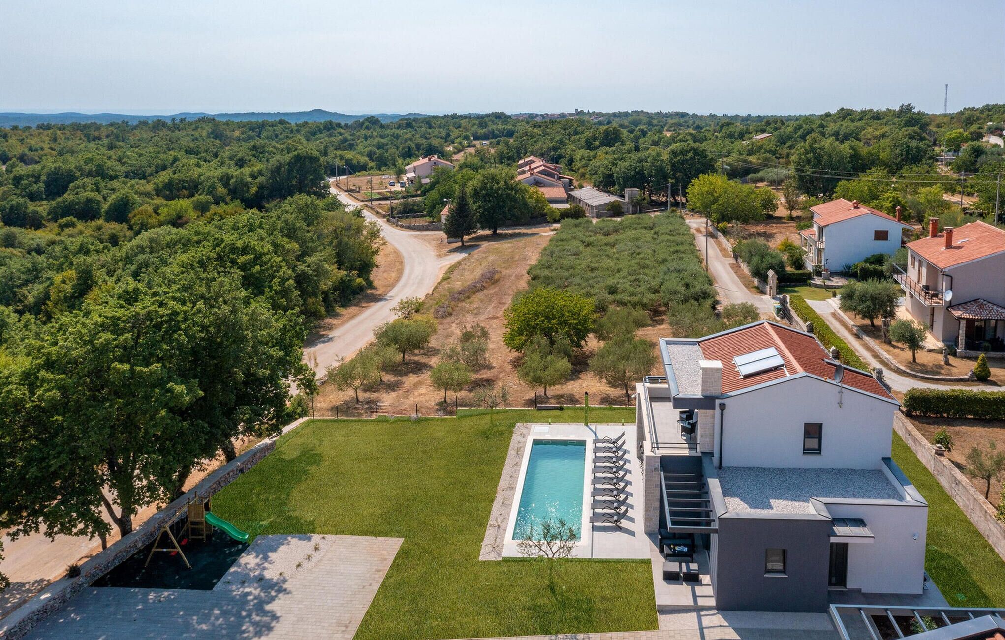 Zona residencial amb piscina, àrea de jocs i cases amb teulades vermelles.