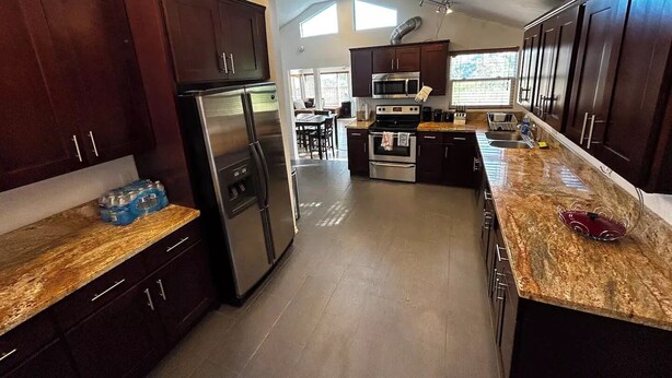 Una cocina moderna con armarios de madera oscura, electrodomésticos de acero inoxidable y encimeras de granito, además de una isla central.