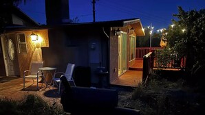 Una casa con terraza de madera, mobiliario exterior y una entrada iluminada.