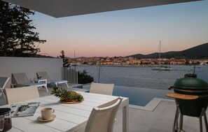 A terrace with a table, chairs, a grill, and a view of a waterfront cityscape at dusk. - Gorgeous home in Vela Luka (Vela Luka)