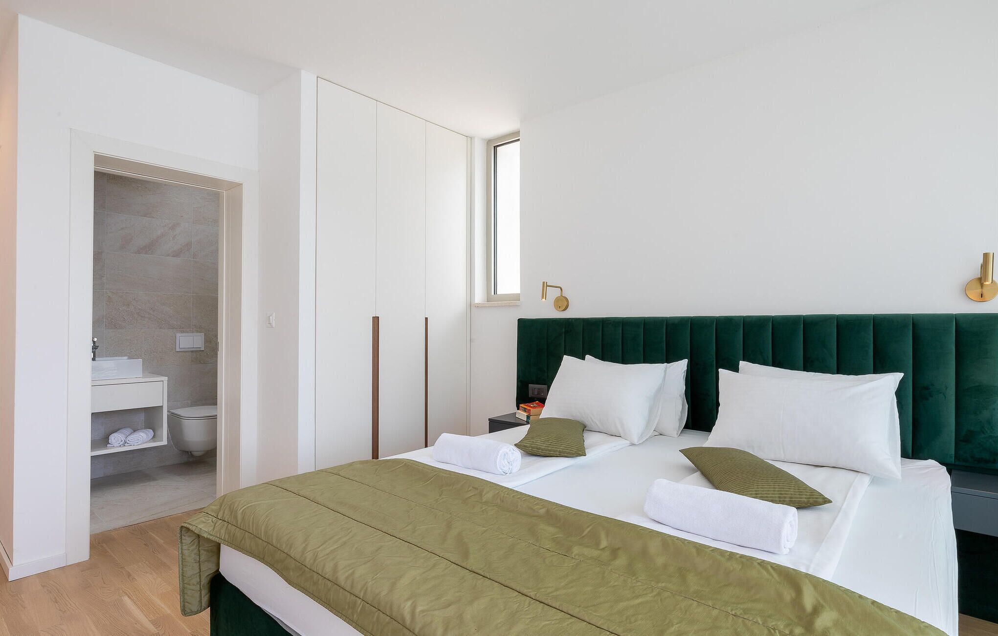 Ein Hotelzimmer mit Bett, Nachttisch, Fenster und einem durchgehenden Türbogen erreichbarem Badezimmer.