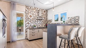 Eine moderne Küche mit einem gemusterten Rückwand, einer zentralen Kochinsel inklusive Barhocker und Blick ins Freie durch ein Fenster.