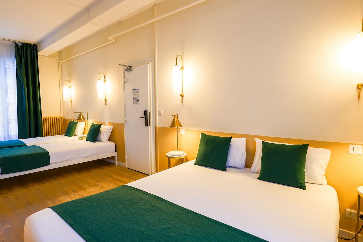 Une chambre d’hôtel avec deux lits, un plancher en bois et une porte dotée d’un interrupteur pour la lumière.