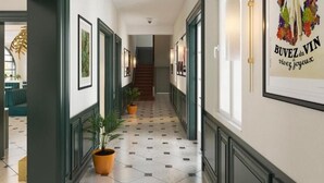 Un couloir aux murs ornés de tableaux encadrés, agrémenté de plantes en pot et doté d’un sol carrelé.