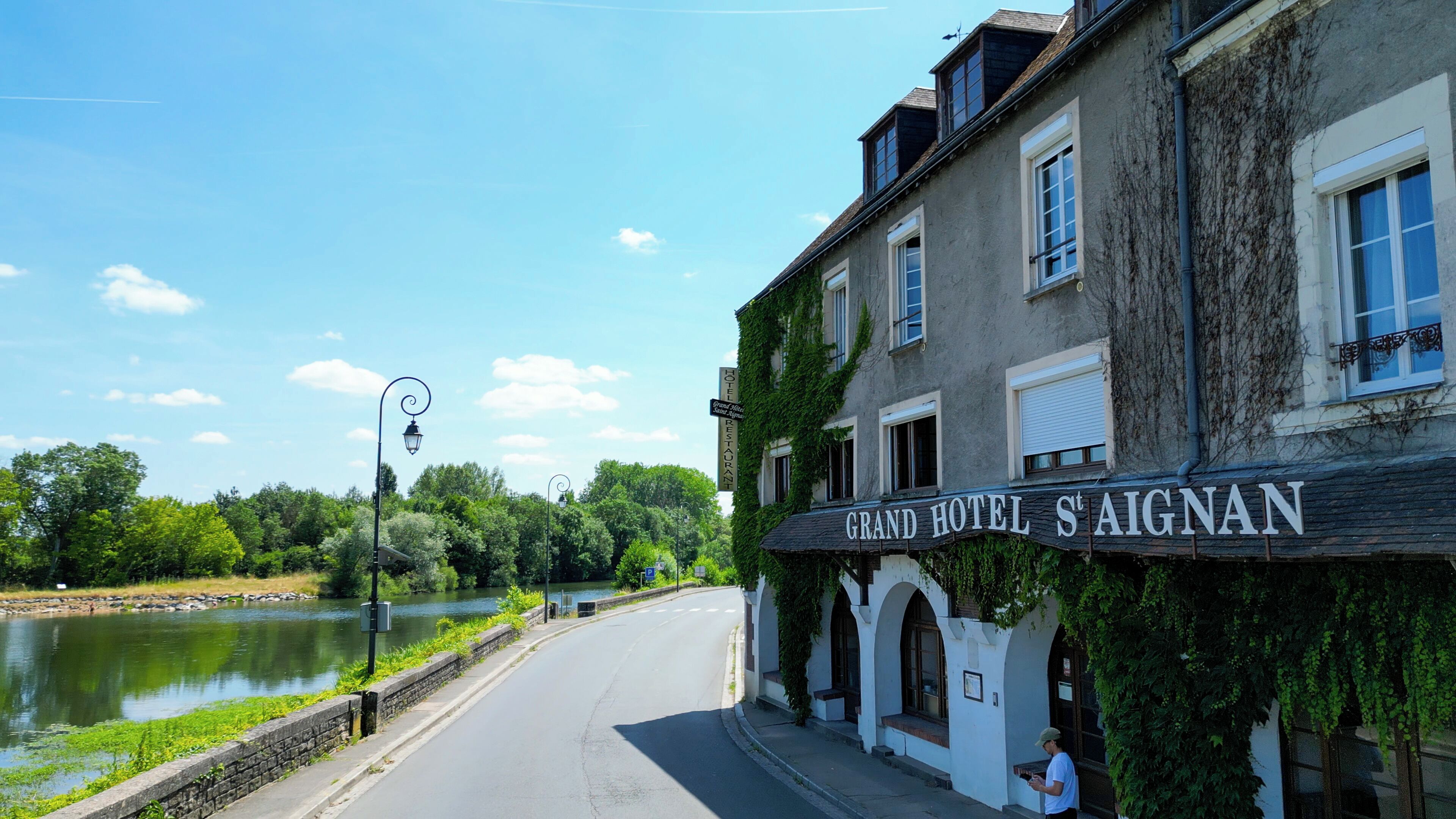 A historic building with a sign reading "Grand Hotel St. Aignan" and a river in the background.