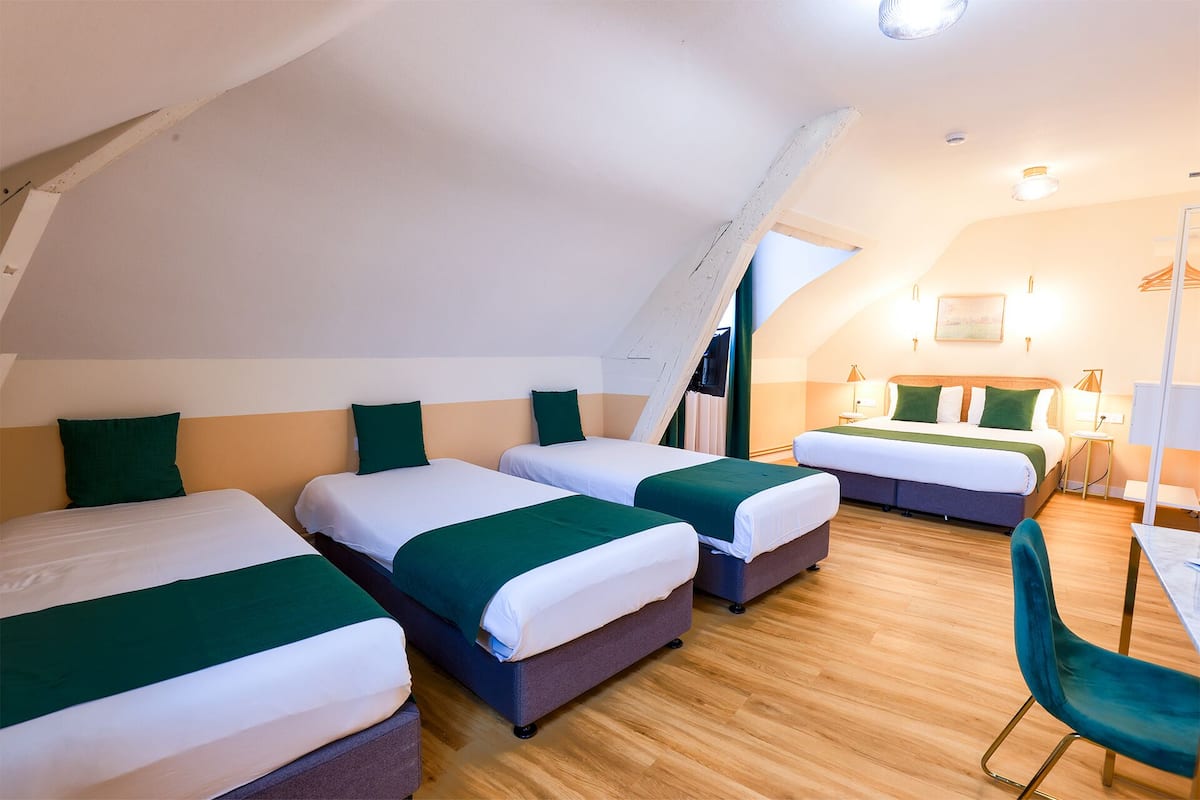 Une chambre d’hôtel avec trois lits, un bureau et une chaise.