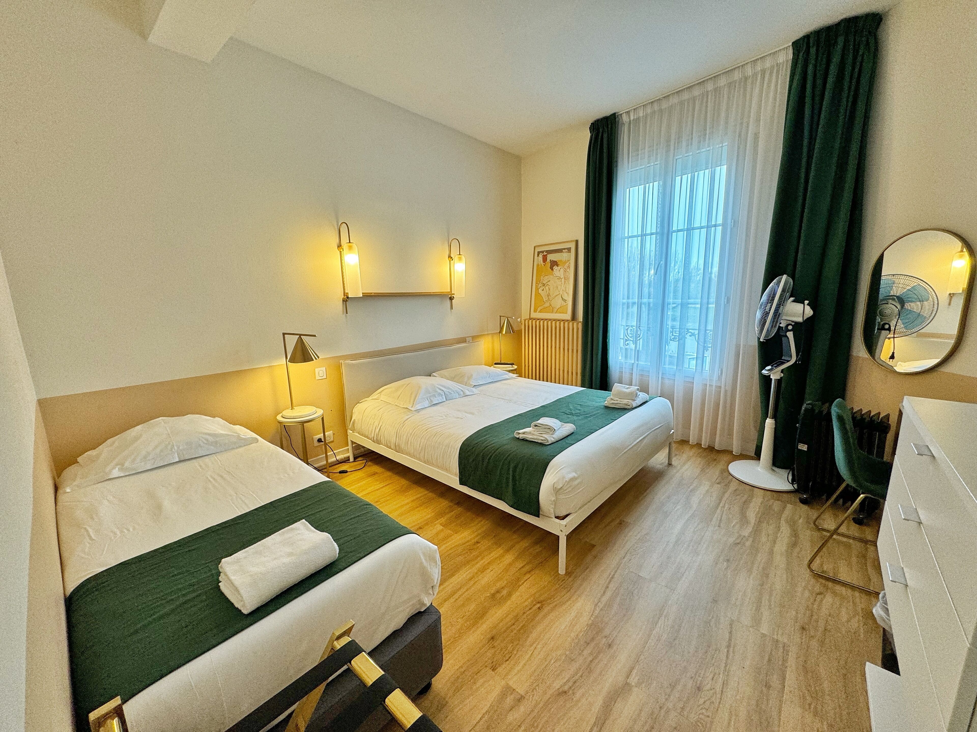 A hotel room with two beds, a desk, a chair, a mirror, and a window with curtains.