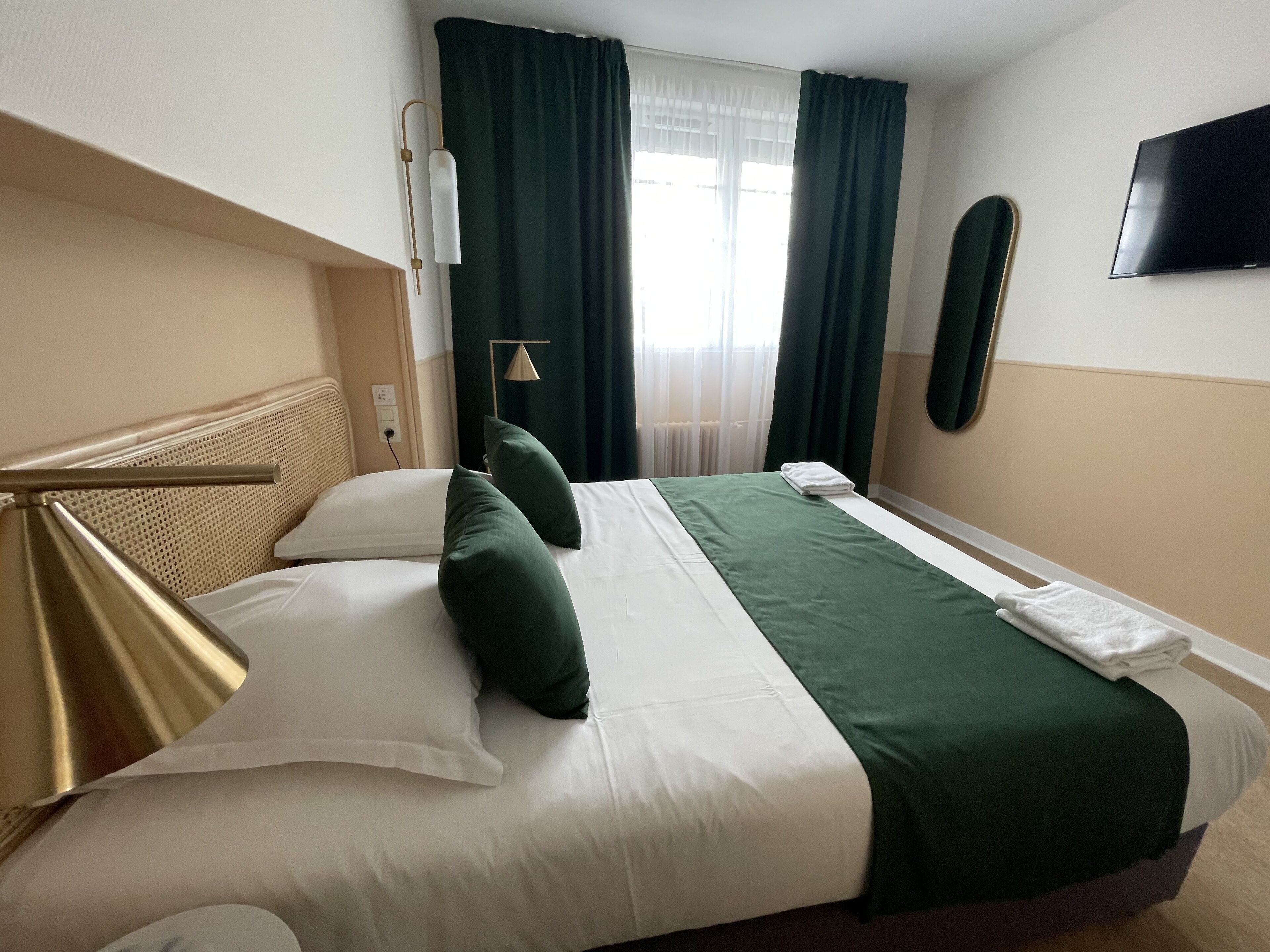 Une chambre d’hôtel avec un grand lit, un téléviseur à écran plat fixé au mur et une fenêtre avec des rideaux.