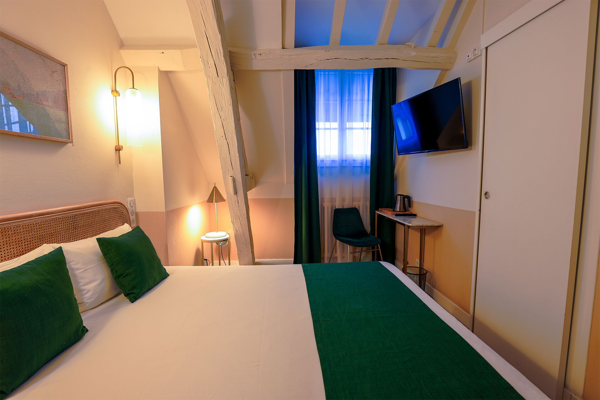 A hotel room with a bed, a desk, a chair, a TV, and a window with curtains.