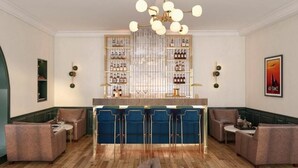 Un espace bar avec des tabourets bleus, un meuble à bouteilles et un lustre.