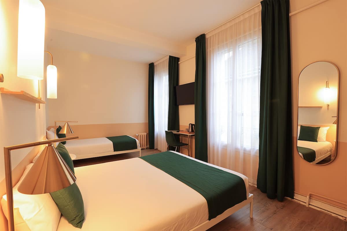 Une chambre d’hôtel avec un lit, un bureau, une chaise, une télévision et un miroir.