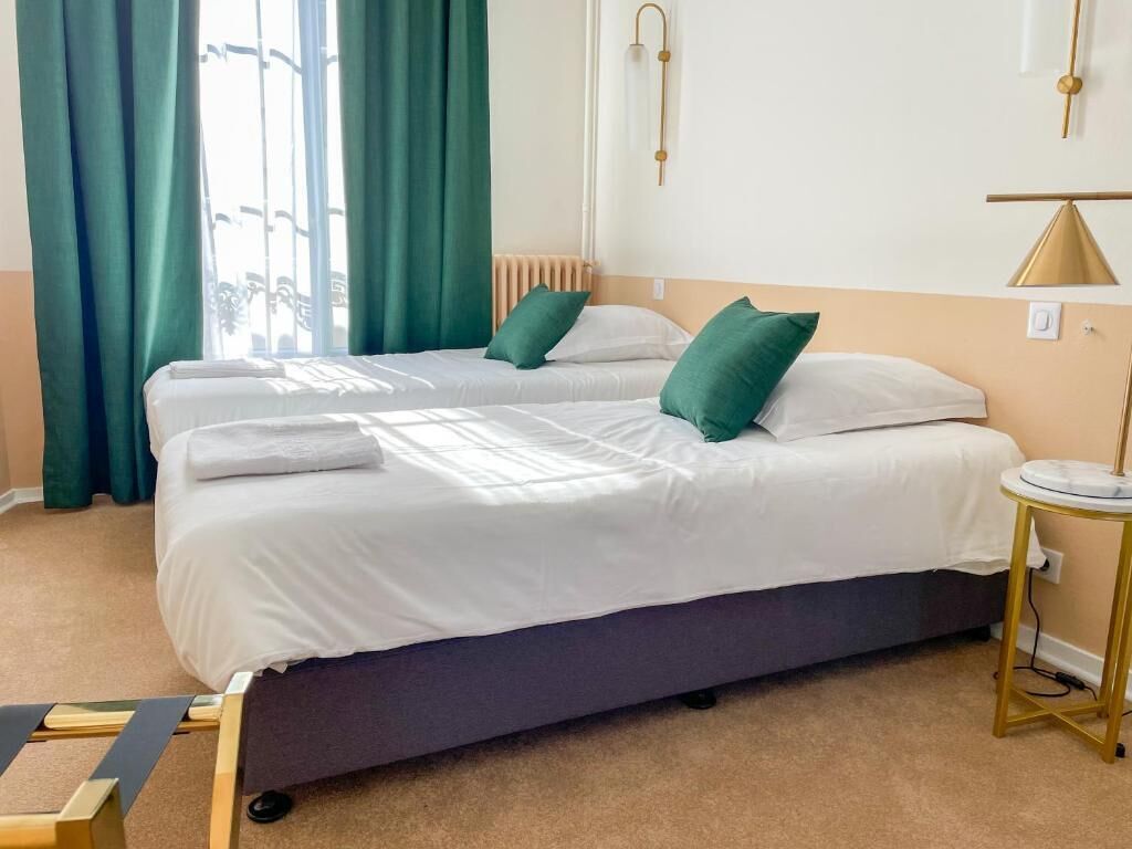 Ett hotellrum med en säng, gröna gardiner, ett nattduksbord och en lampa.