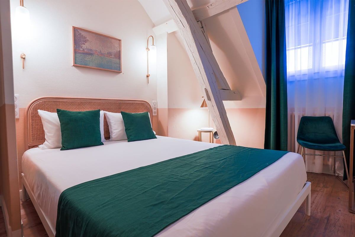 Une chambre d’hôtel moderne avec un grand lit, un tableau au mur et une vue sur l’extérieur par une fenêtre.