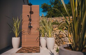 Relax in a serene outdoor shower surrounded by lush greenery and a natural stone backdrop.