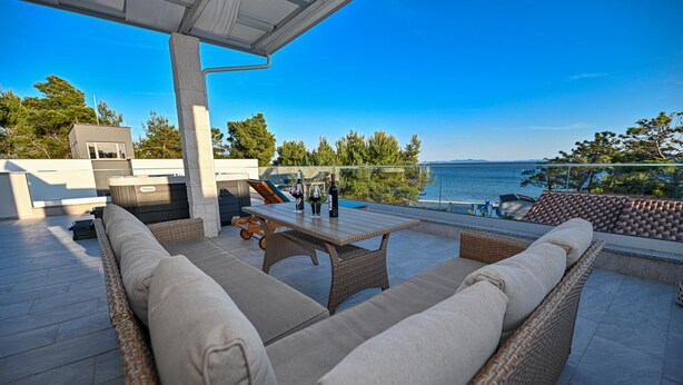 Eine Dachterrasse mit einer Couch, einem Tisch und Stühlen mit Blick auf ein Gewässer und viel Grün.