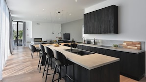 Une cuisine moderne dotée d’un îlot central, de tabourets de bar et d’un grand panneau de protection noir.
