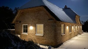 Ein Steinhaus mit schneebedecktem Dach und mehreren beleuchteten Fenstern.