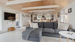 Ein modernes Wohnzimmer mit einem grauen Ecksofa, einem Flachbildfernseher und einer Holzzieldecke.