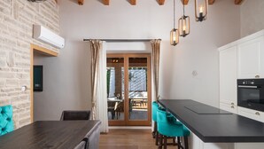 Une cuisine moderne avec un plan de travail noir, des armoires blanches et un four Bosch. On y trouve un coin repas avec une table en bois et des chaises turquoise. Une porte-fenêtre coulissante donne accès à un espace extérieur aménagé avec une table et des chaises.