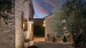 Un bâtiment en pierre doté d’une cour pavée, de plantes en pot et d’un arbre.
