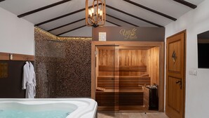 Un sauna avec des bancs en bois et une porte en verre, une baignoire blanche remplie d’eau et une serviette suspendue à un porte-serviettes.