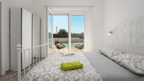 A bedroom with a bed, a balcony with chairs, and a view of the outdoors. - Beautiful new Villa with private pool ideal for vacation for couples or a family (Krnica)