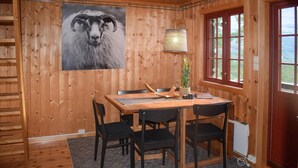 Un interno in legno con un tavolo da pranzo, sedie, un quadro incorniciato raffigurante un ariete e una finestra con vista.
