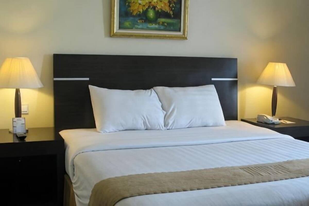Ein Hotelzimmer mit einem Bett, zwei Nachttischen mit Lampen, einem Bild an der Wand und einem Telefon auf einem der Tische.