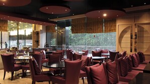 Un restaurant moderne avec des tables rondes et des sièges rembourrés, de grandes fenêtres et une vue sur la verdure.