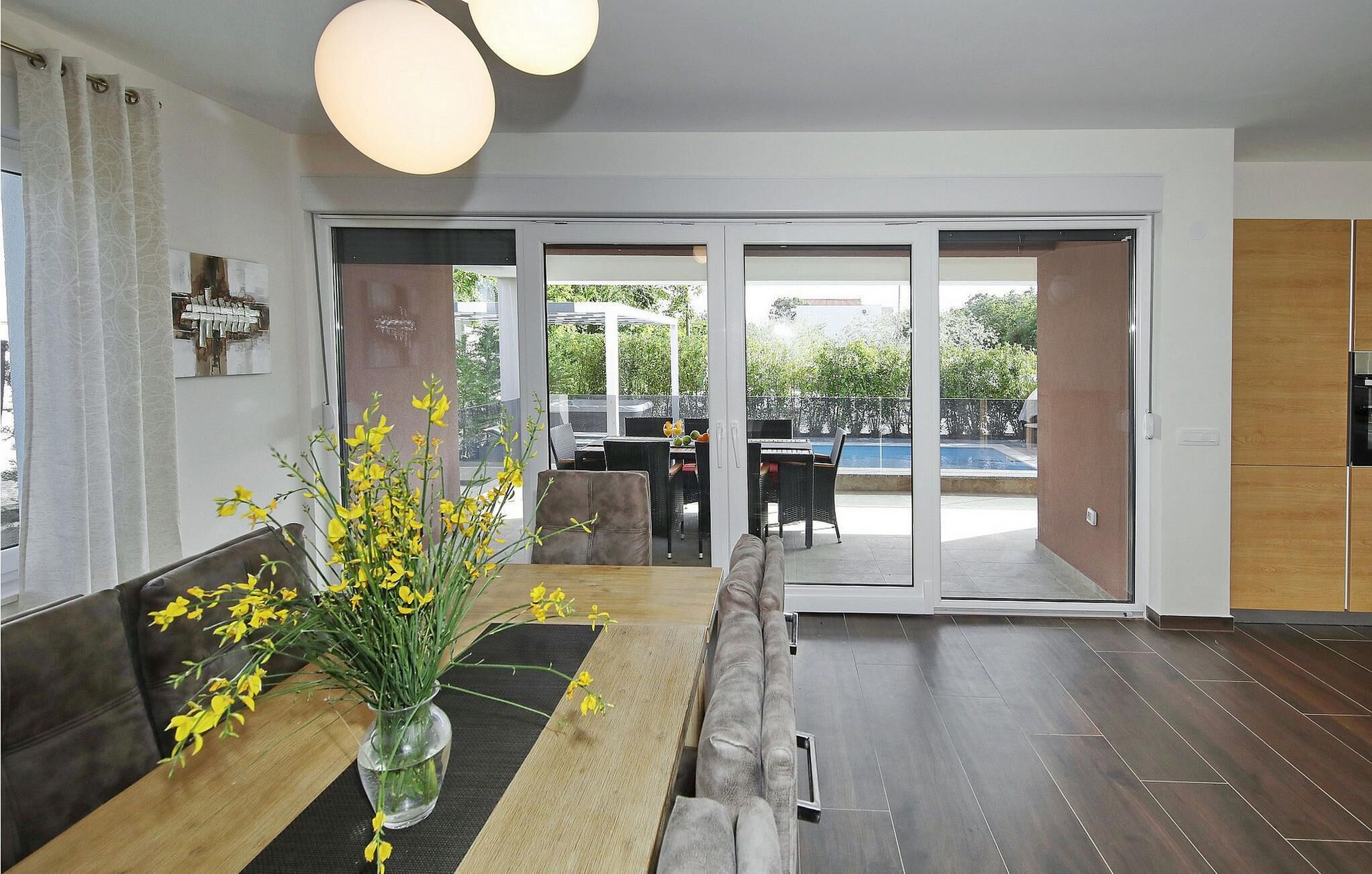 A modern living room with a dining area, large windows, and a view of a pool and greenery.
