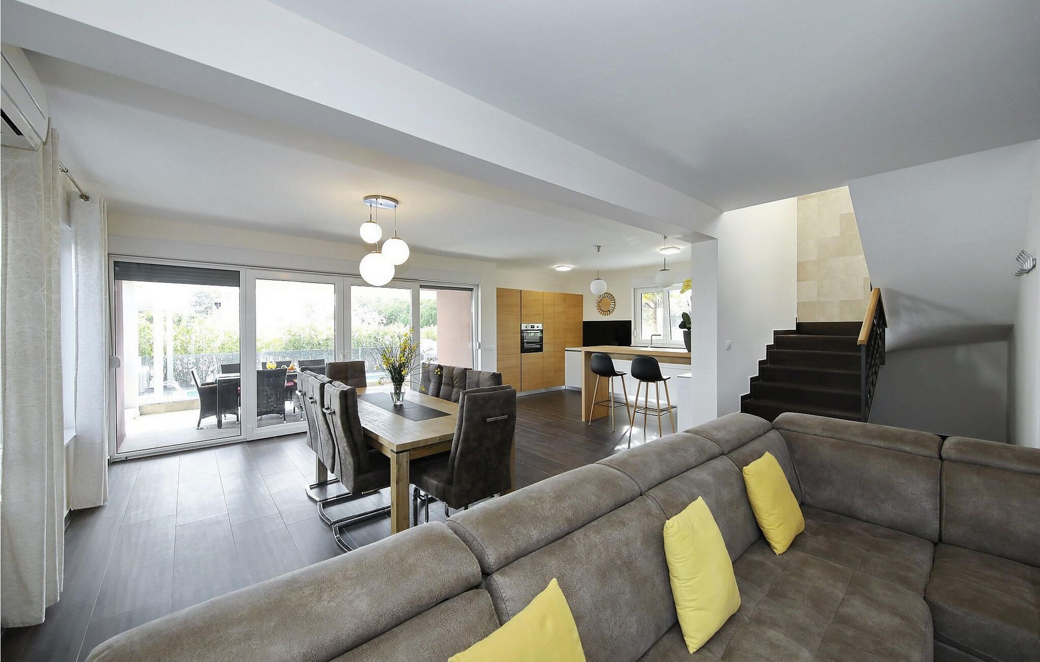 A modern living room with a sofa, dining area, kitchen, and staircase.