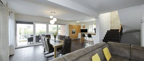 A modern living room with a sofa, dining area, kitchen, and staircase.
