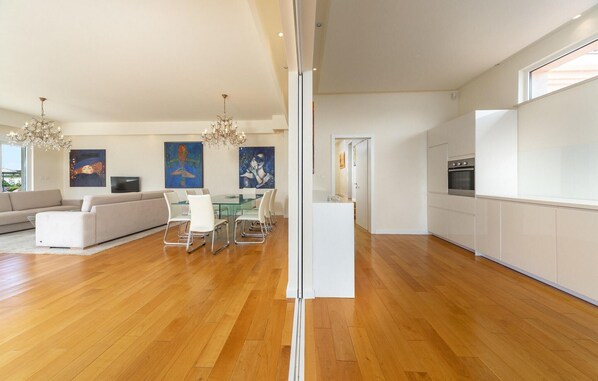 Una sala de estar moderna con sofá, mesa de comedor y sillas, una cocina con armarios y electrodomésticos, y obras de arte en las paredes.