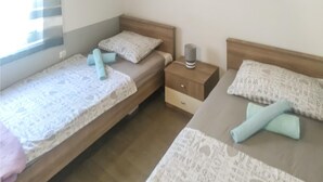 Una habitación con dos camas individuales, cada una con una almohada y una toalla enrollada. Hay una mesita de noche con una lámpara entre las camas.
