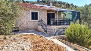 Una casa de piedra con techo de tejas, un balcón con barandilla de metal y una ventana pequeña.