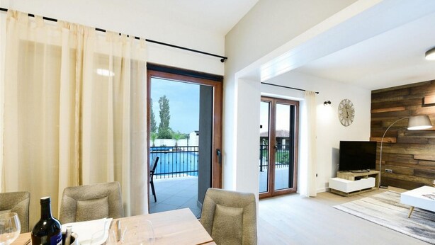A modern living room with a wooden dining table, two chairs, a TV, and a wooden accent wall. - Lovely home in Policnik with sauna (Policnik)