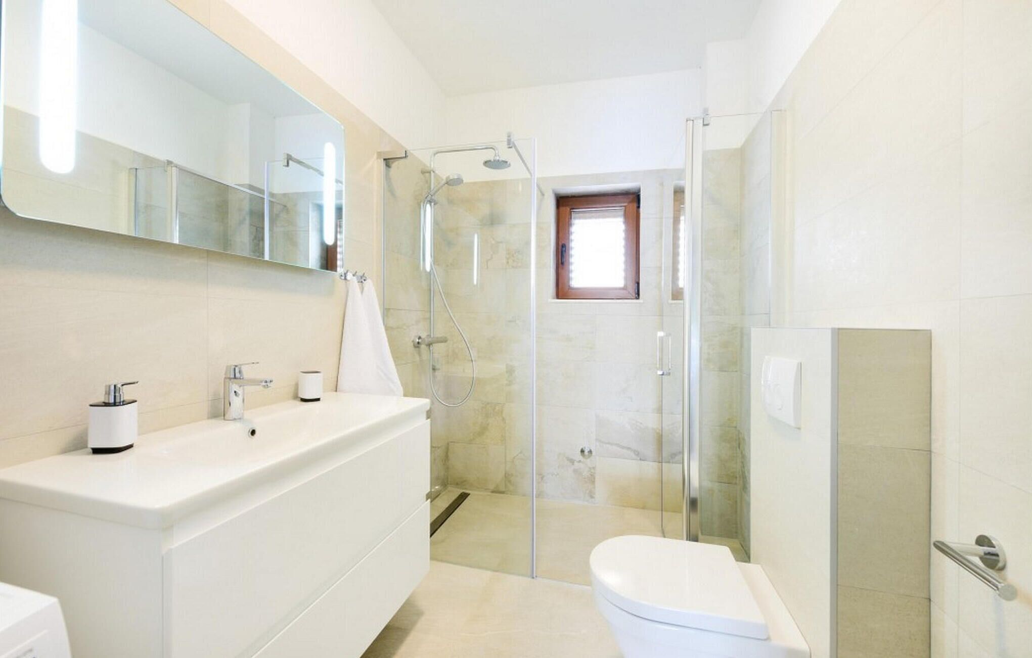 Een moderne badkamer met een douchecabine van glas, een witte wastafel en een toilet.