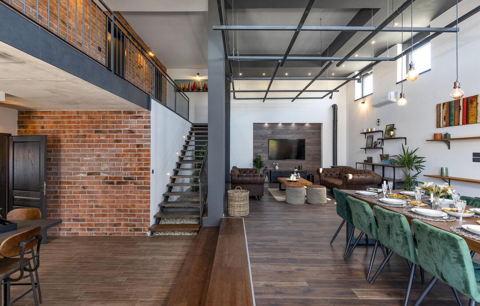 Un vaste loft doté de murs en briques apparentes, d’une mezzanine et d’un coin repas avec une longue table et des chaises.