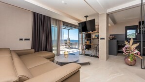 Una sala de estar moderna con un sofá, una mesa de centro y una estantería. Hay un balcón con vistas al mar.