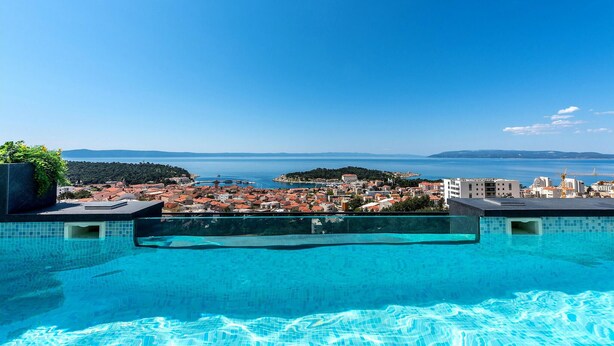 Una piscina con agua cristalina azul, con vistas a un pueblo costero con edificios y al mar.