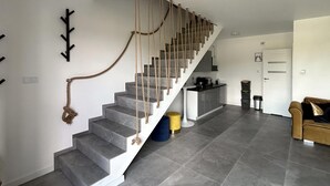 Una escalera moderna con barandilla de cuerda, una zona de cocina con mostrador tipo bar, y un espacio de estar con sofá.