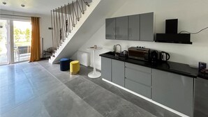 Una cocina moderna con gabinetes grises, una encimera negra y un microondas integrado. Se aprecia una escalera con un diseño original y una pequeña mesa redonda con una vela.